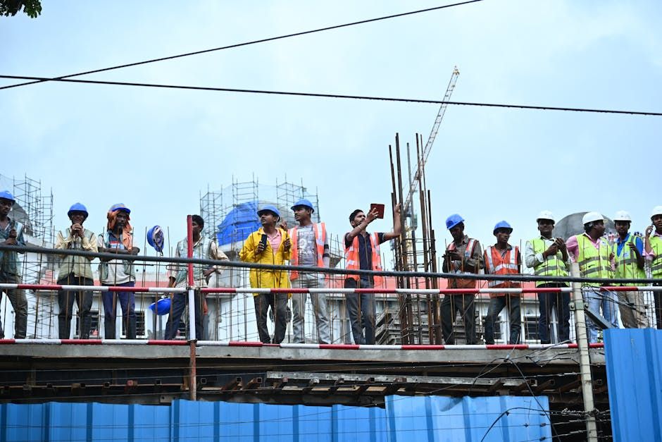 Group of construction workers standing on scaffolding wearing safety gear, hard hats, and vests.